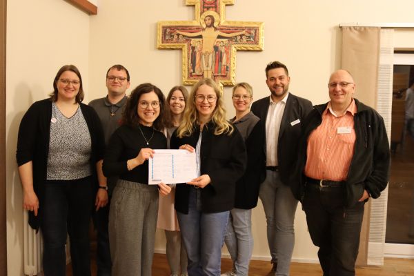 7 Personen stehen mit einer Unterschriftenliste vor einem Kreuz, lächeln in die Kamera