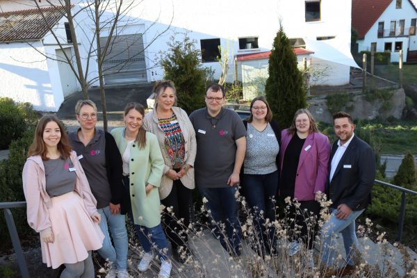 8 Personen stehen vor einem Trebbengeländer in der Natur