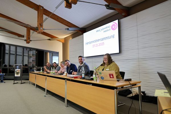 5 Personen sitzen, vor ihnen Mikrofone und Wasserflaschen auf einem Tisch