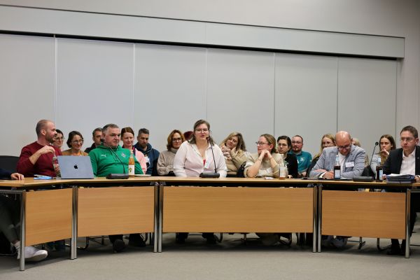 30 Personen sitzen im Sitzungssaal, erste Reihe mit Tischen