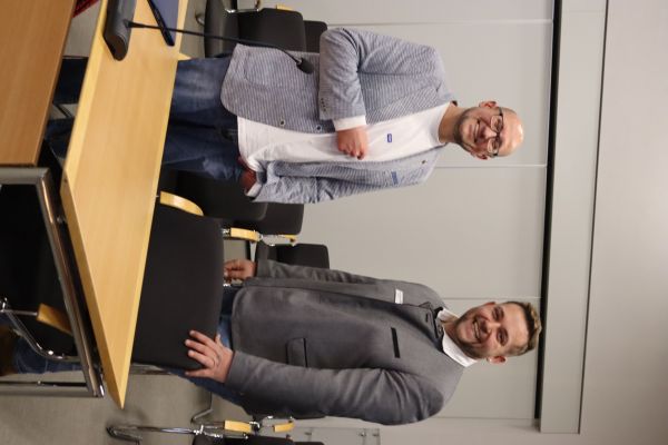 2 Personen stehen nebeneinander und lächeln in die Kamera