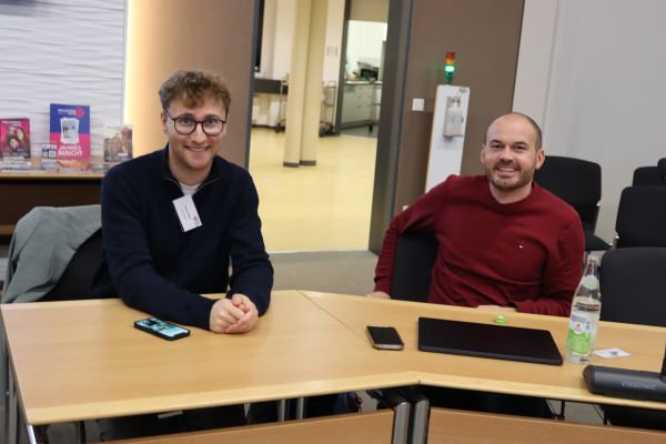 2 Personen sitzen nebneinander am Besprechungstisch und lächeln