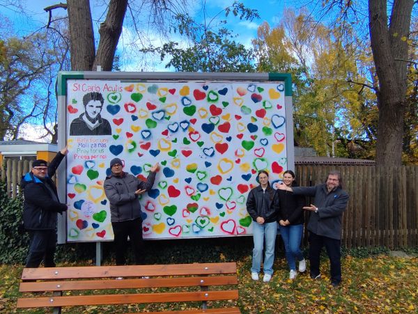 4 Personen präsentieren eine Plakatwand von St. Carlo Acutis
